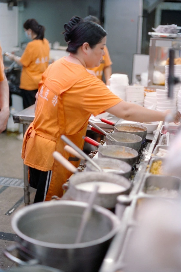 Woman in orange shirt preparing food in kitchen.